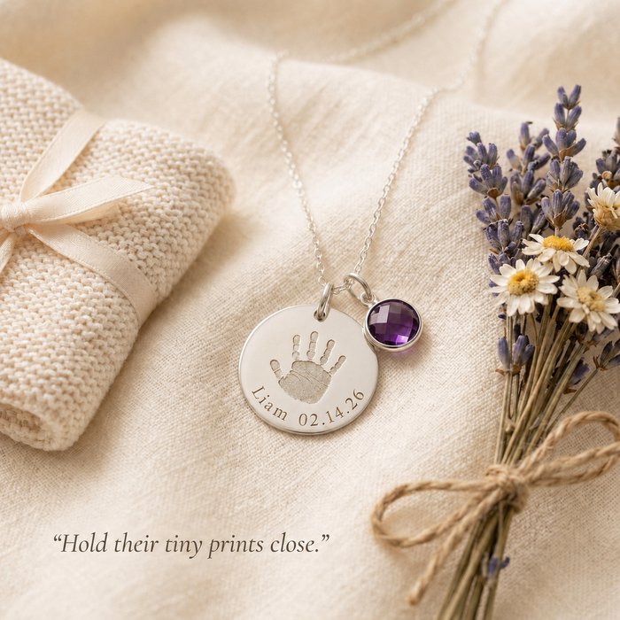 Baby handprint memorial necklace with birthstone charm styled on soft fabric with lavender and remembrance message.