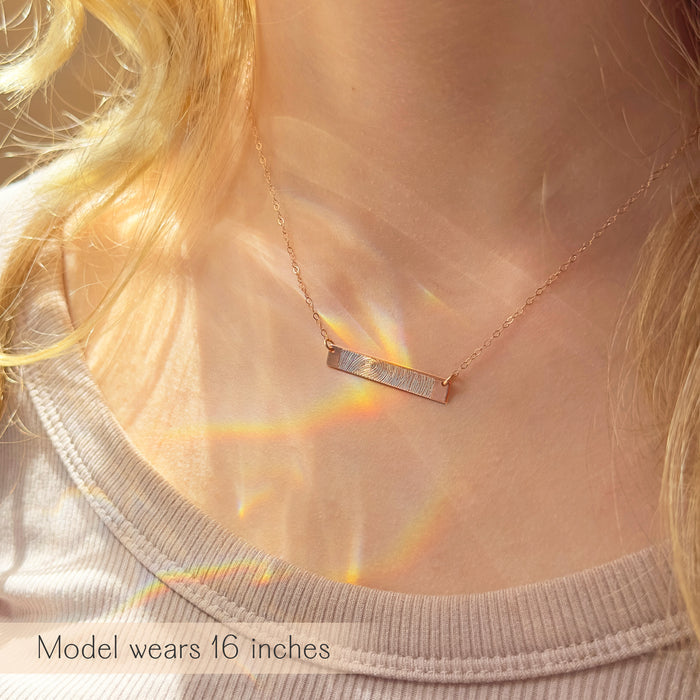 Model wearing a personalized fingerprint bar necklace layered on the neckline, delicate horizontal bar pendant engraved with fingerprint detail, minimalist everyday jewelry styled in natural light