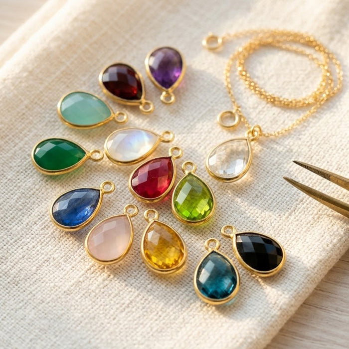 Teardrop birthstone charms in multiple gemstone colors displayed on soft fabric, designed as add-on charms for Danique necklaces and bracelets.