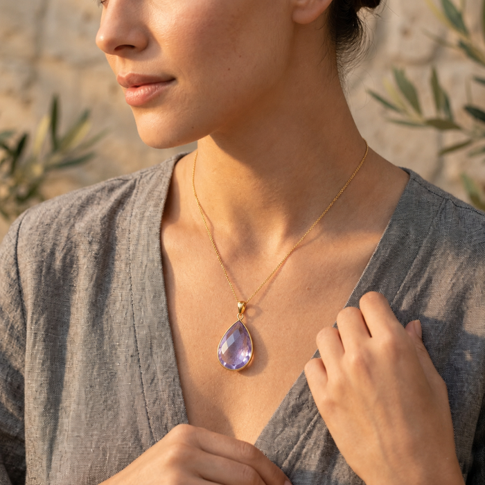 Model wearing dainty alexandrite teardrop necklace in gold with soft lavender-purple June birthstone.