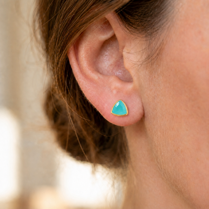 Close-up of an aqua chalcedony triangle stud earring worn on the ear, showing the dainty 8mm gemstone size.