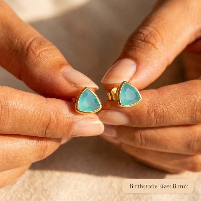Aqua chalcedony triangle stud earrings held between fingers, showing the 8mm blue-green gemstones in gold settings.