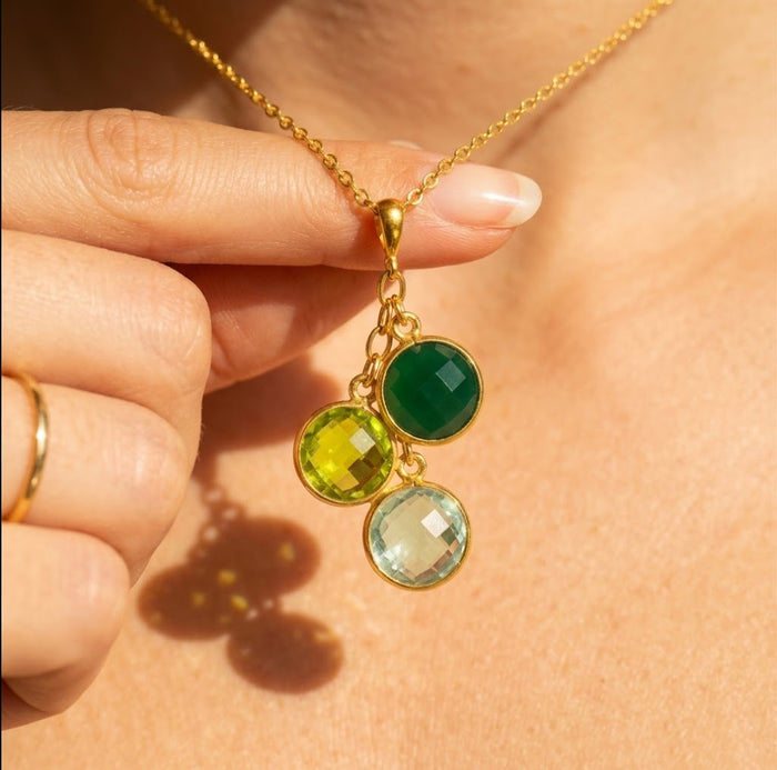 Family birthstone cluster necklace with green gemstones in yellow gold worn on model