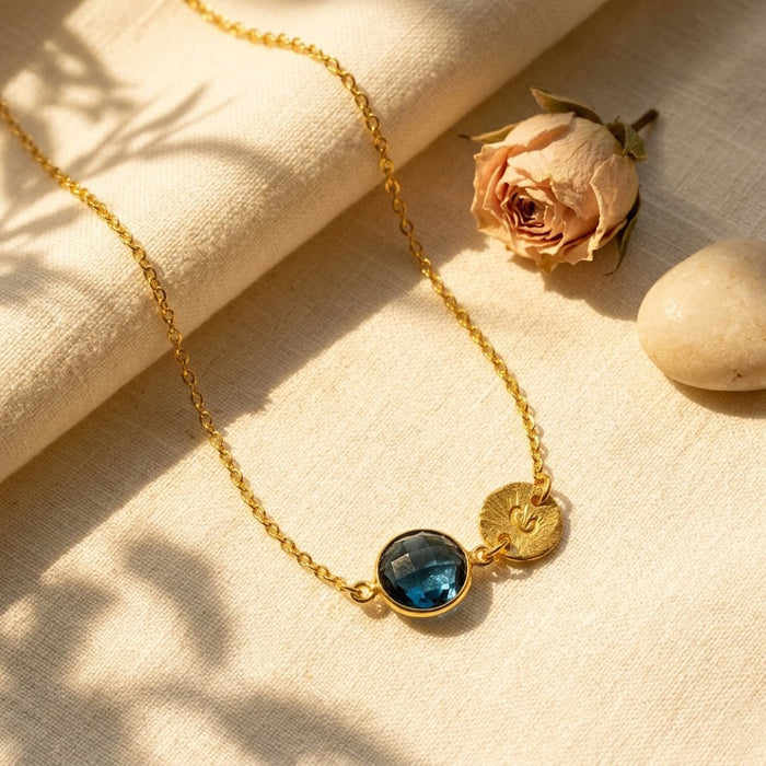 Dainty gold blue kyanite necklace with September birthstone charm and personalized initial disc on beige fabric