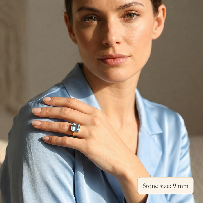 Blue topaz December birthstone ring worn on model in a light blue blouse with text overlay reading stone size 9 mm, showing the scale of the cushion cut gemstone ring for birthdays, holiday gifts, anniversary jewelry, minimalist style, and December birthstone gifts.