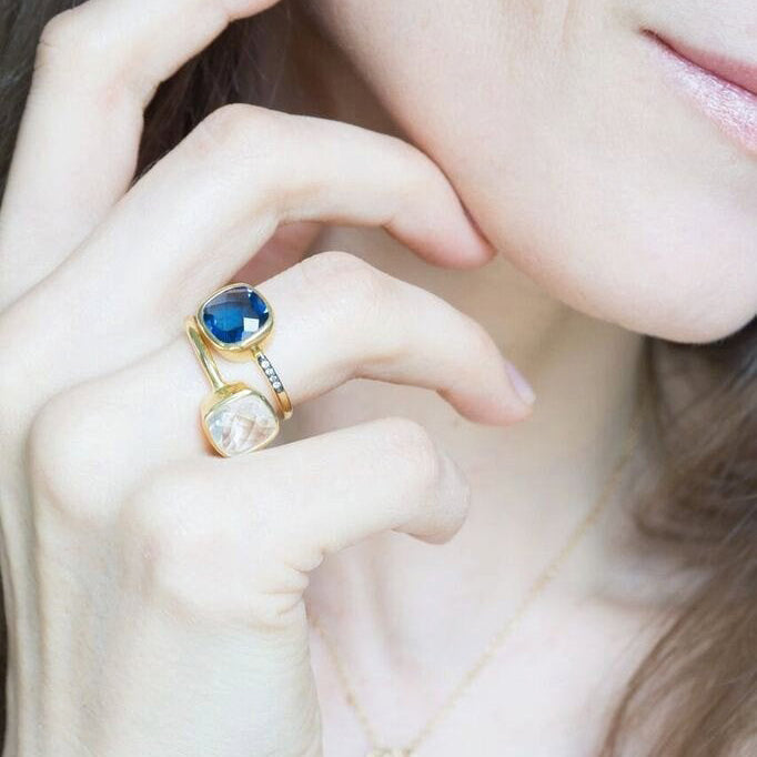 Model is stylishly stacking the cushion pave set gold plated kyanite birthstone ring with the cushion gold plated clear quartz ring. Stackable, versatile birthstone rings