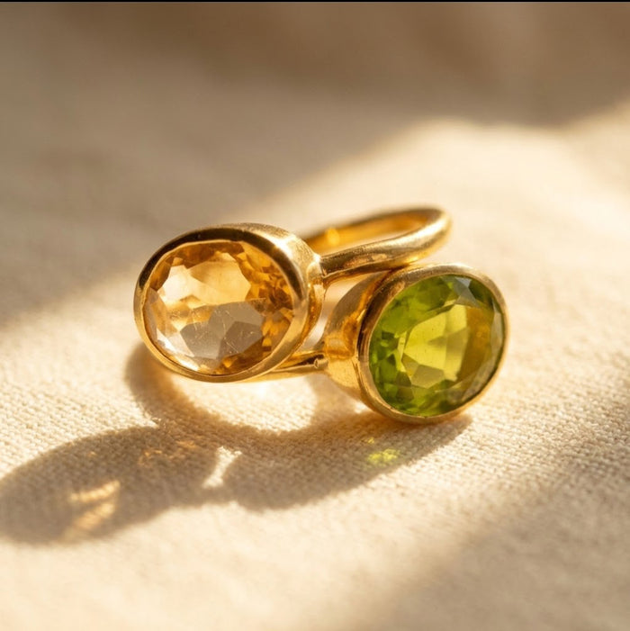 Citrine and peridot birthstone ring with two oval gemstones in gold on beige fabric