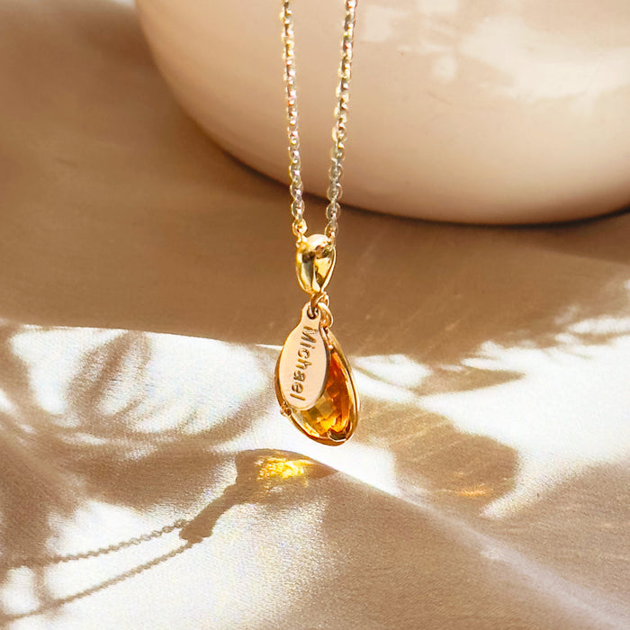 Citrine November birthstone necklace featuring a warm golden teardrop citrine gem in a prong-style setting, paired with a small oval name tag engraved with “Michael” on a delicate gold-filled chain, sunlight reflecting on the satin background to highlight the rich yellow stone. Personalized citrine pendant makes a meaningful November birthday gift for mom, grandma, daughter or best friend, a custom engraved keepsake she can wear every day.