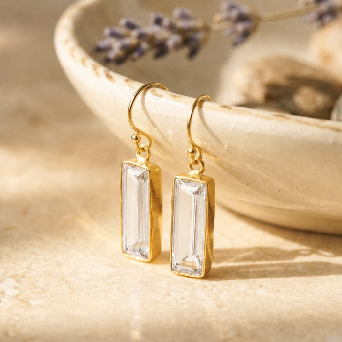 Clear quartz bar drop earrings in yellow gold vermeil displayed on a ceramic bowl in warm natural sunlight.