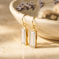 Clear quartz bar drop earrings in yellow gold vermeil displayed on a ceramic bowl in warm natural sunlight.