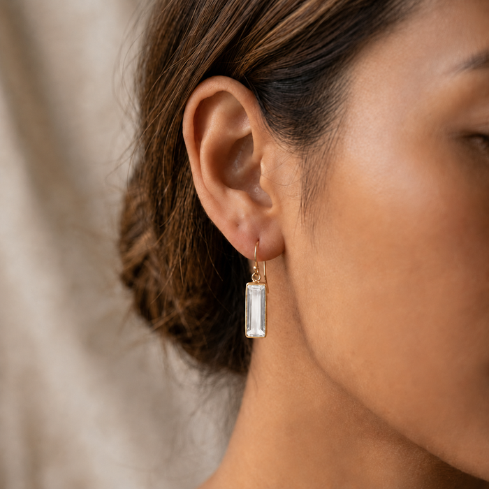 Close-up of clear quartz drop earrings in gold on a model’s ear with soft neutral lighting.