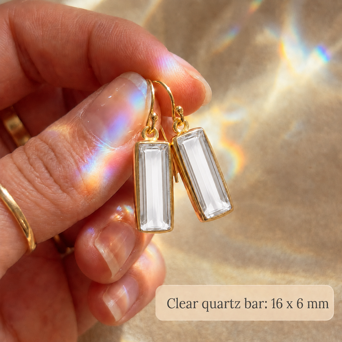 Clear quartz earrings held in hand, showing the 16 x 6 mm baguette-cut gemstone size.