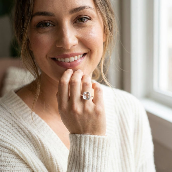 Woman wearing cushion cut clear quartz gold ring, 9mm square transparent gemstone in modern bezel setting, April birthstone jewelry styled in natural light, minimalist diamond alternative ring, elegant gold stacking birthstone ring, handcrafted fine jewelry for women, square bezel set white quartz statement ring gift