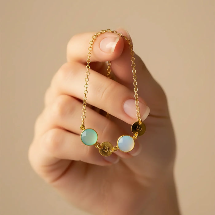 Mom’s custom birthstone initial bracelet held delicately between fingers, featuring a dainty gold chain with pastel bezel-set gemstones and tiny round letter discs spelling children’s initials for a meaningful family design. Minimalist personalized bracelet perfect for everyday wear or stacking with other bangles, a sentimental Mother’s Day, birthday, Christmas or new mom gift celebrating kids’ birthstones and initials in elegant, modern style.