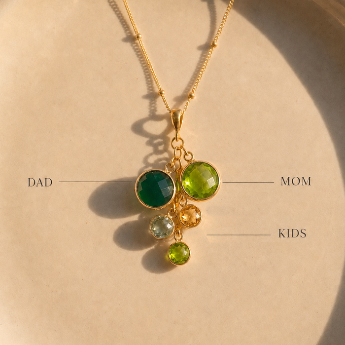 Close-up of gold cascade birthstone necklace with green family stones labeled for Dad, Mom, and kids.