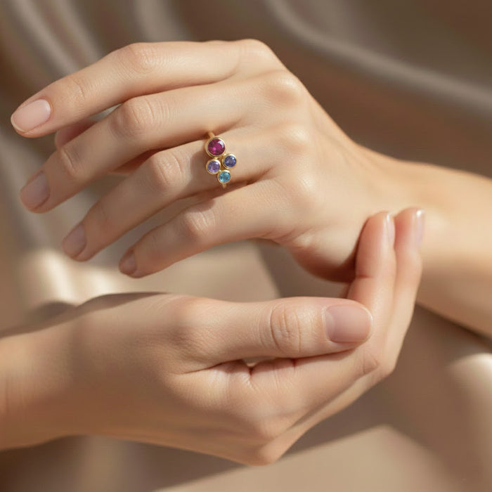 dainty three stone birthstone ring shown stacked with minimalist bands on woman’s hand, personalized gemstones representing her children in vibrant colors, gold vermeil band offering elegant modern style, customizable family ring perfect for Mother’s Day or birthday gifting, crafted in sterling silver or gold vermeil with high-quality stones, sentimental jewelry piece for moms who cherish family connections