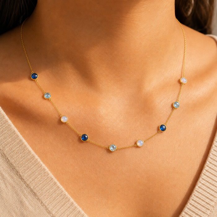 Woman wearing a personalized natural birthstone station necklace with blue and white gemstones in yellow gold