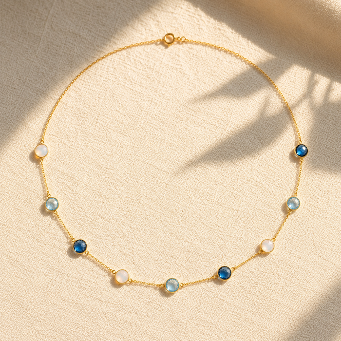 Long birthstone station necklace with blue and white natural gemstones arranged on warm beige fabric