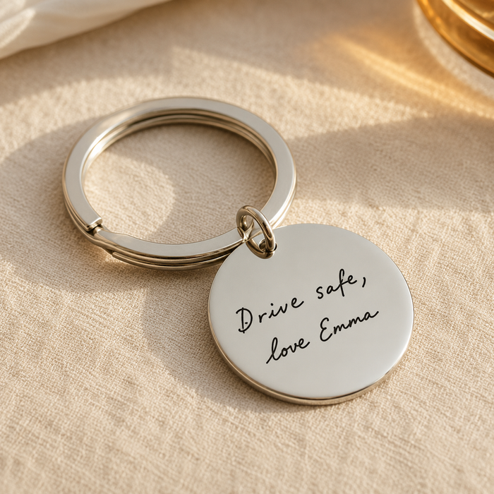 Personalized round stainless steel keychain engraved with custom handwriting that says Drive safe, love Emma.