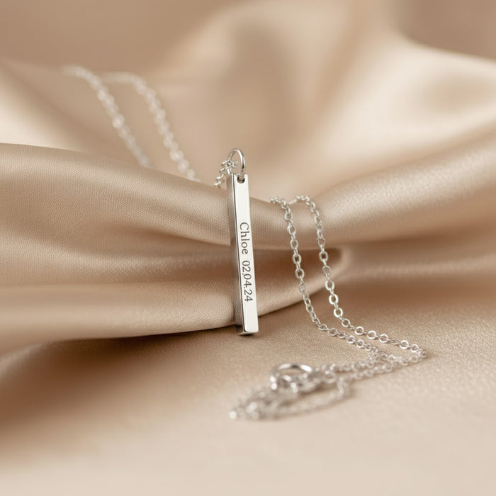 A minimalist sterling silver bar pendant etched with exact latitude longitude necklace details, styled on a soft backdrop with prism light. This slim GPS coordinates necklace turns a special place—first date, proposal spot, new home—into elegant location jewelry. Deep laser text runs along one face of the bar for a modern engraved coordinate bar look; perfect as a travel keepsake gift or anniversary memento with custom map coordinates and adjustable chain length.