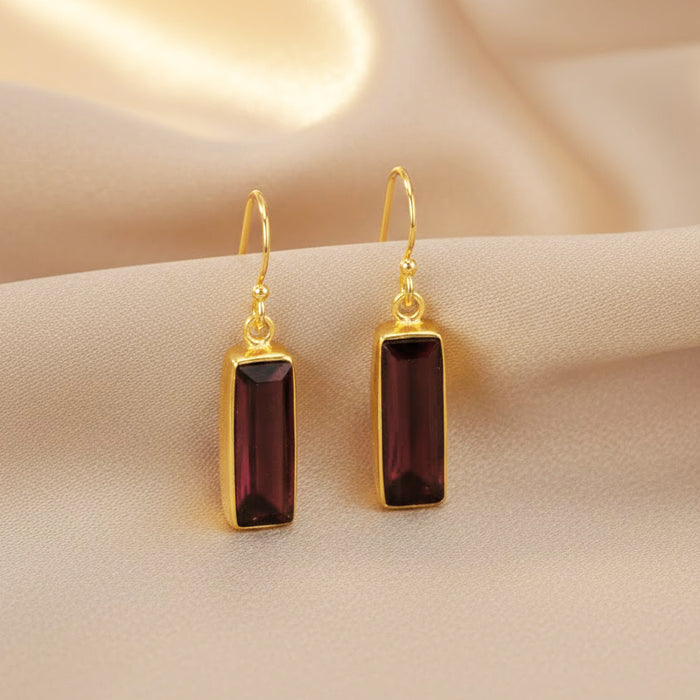 Close-up of garnet baguette drop earrings highlighting deep red gemstone color and gold setting. January birthstone earrings designed with a sleek rectangular silhouette. Elegant gemstone earrings perfect for anniversaries, birthdays, or meaningful everyday jewelry.