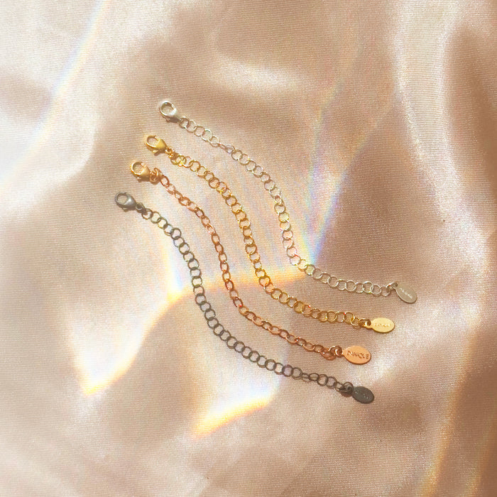 Necklace extender chains in gold, silver, and rose gold displayed on satin fabric background. Jewelry accessory adds 1–6 inches to necklace or bracelet for layering styles. Popular gift upgrade for birthdays, Christmas, or bridesmaids.