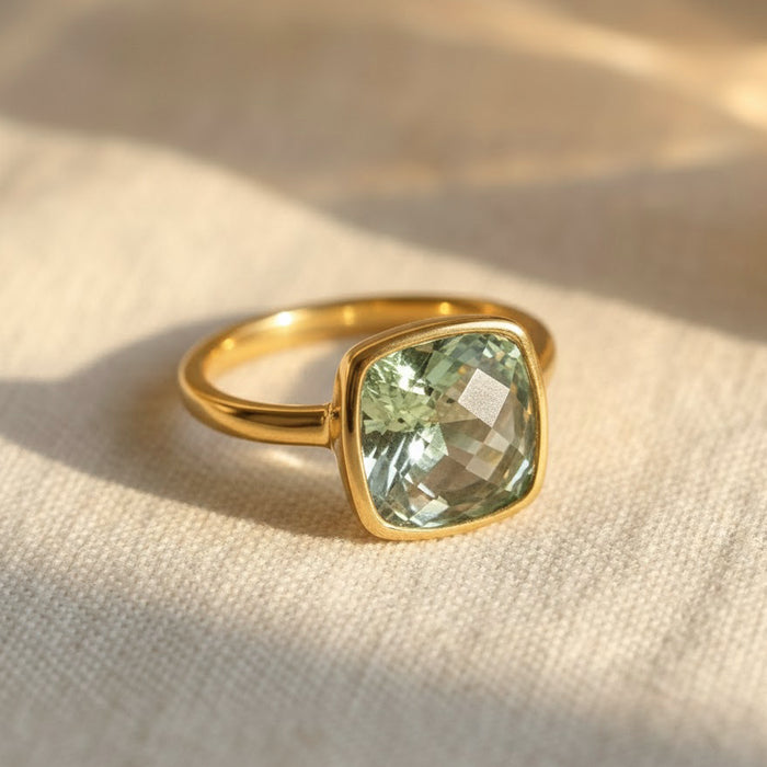 Cushion cut green amethyst ring in polished yellow gold bezel setting resting on neutral linen fabric, featuring a 9mm square prasiolite gemstone with soft sage green glow, February birthstone ring for women, minimalist modern fine jewelry, dainty gold gemstone ring, handcrafted artisan birthstone jewelry, elegant stacking ring, square bezel set green quartz ring gift for her