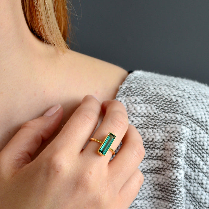 A person wears a green tourmaline gemstone ring on their hand. Green tourmaline gemstone jewelry, bar ring, handcrafted May birthstone ring, deep green tourmaline, minimalist style, green tourmaline in gold, silver green ring, boho chic jewelry, artisan green tourmaline ring, stacking gemstone ring, unique green jewelry, green tourmaline statement piece