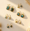 Labradorite earrings in multiple styles arranged in warm sunlight, showing blue-green flash gemstones in gold settings, including teardrop and round drop earrings for everyday wear or gifting.