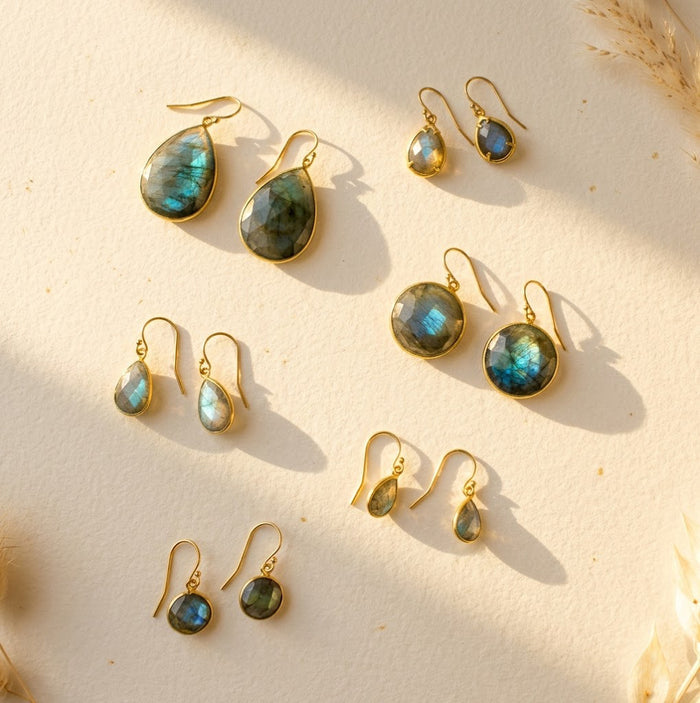 Labradorite earrings in multiple styles arranged in warm sunlight, showing blue-green flash gemstones in gold settings, including teardrop and round drop earrings for everyday wear or gifting.
