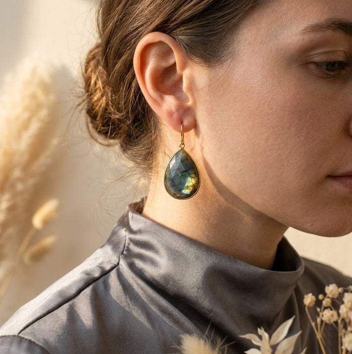 Close-up of model wearing large labradorite drop earrings, highlighting the blue-green flash and elegant teardrop shape for statement gemstone jewelry.