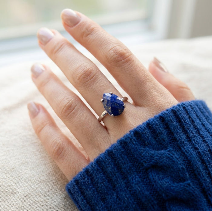 Hand wearing a sterling silver lapis lazuli teardrop ring with faceted blue gemstone and delicate prong setting.
