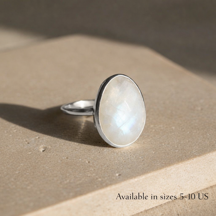 Rainbow moonstone oval ring set in .925 sterling silver, photographed on a neutral stone surface with soft natural light. Bezel-set June birthstone ring featuring a luminous oval moonstone with subtle iridescence. Minimalist moonstone jewelry designed for everyday wear, stacking, and timeless style, available in US ring sizes 5–10 and handcrafted for meaningful gifting.