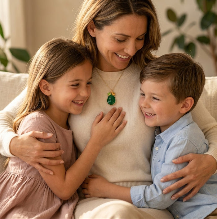 Mother wearing custom birthstone necklace while hugging her children at home