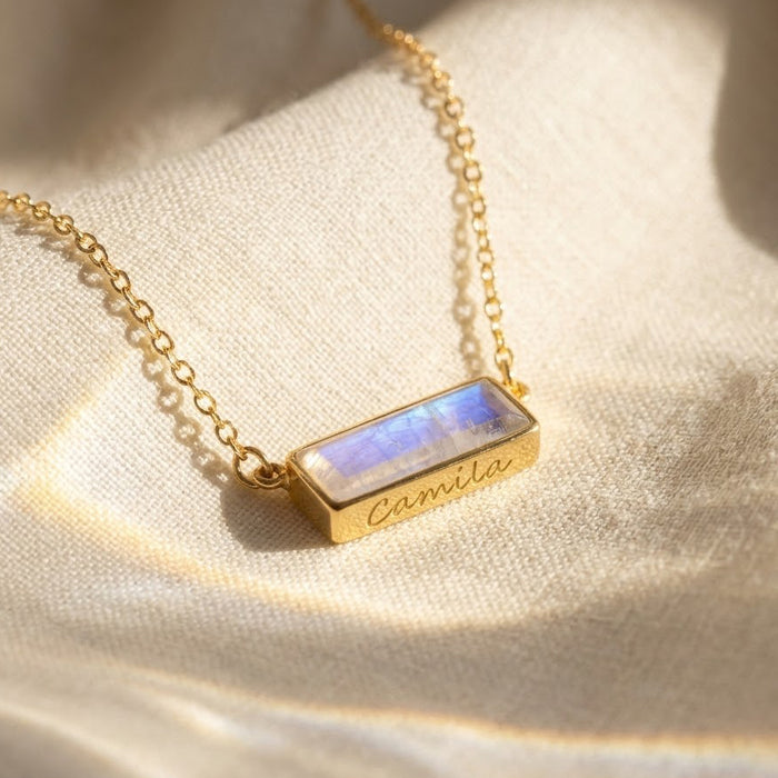 Close-up of a natural moonstone bar necklace on soft fabric, showing the horizontal June birthstone pendant in a gold setting.