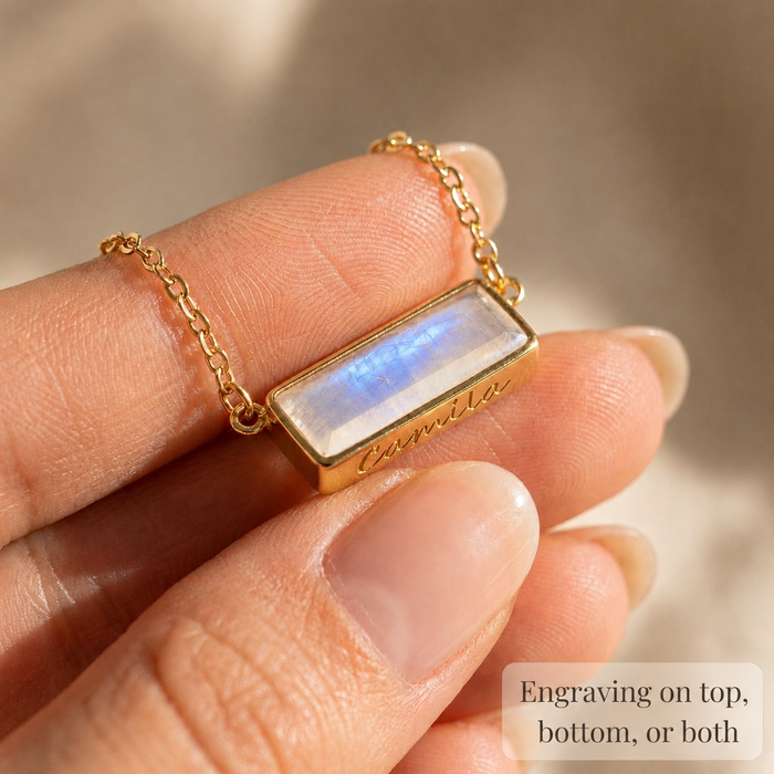 Close-up of a moonstone bar pendant held between fingers with text explaining engraving on the top, bottom, or both sides.
