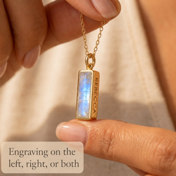 Close-up of a vertical moonstone bar necklace held between fingers with text explaining engraving on the left, right, or both sides.
