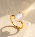 Moonstone teardrop ring in yellow gold with pear rainbow moonstone on warm neutral fabric