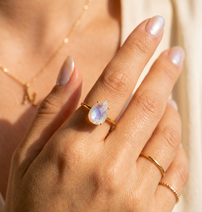 Moonstone teardrop ring worn on hand in warm sunlight with gold band and June birthstone