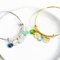 Sterling silver bangle bracelet with name tags in classic font and kyanite, moonston and aqua chalcedony. Single gold bangle bracelet with two name disks and peridot and blue quartz birthstones with names engraved in modern thin font