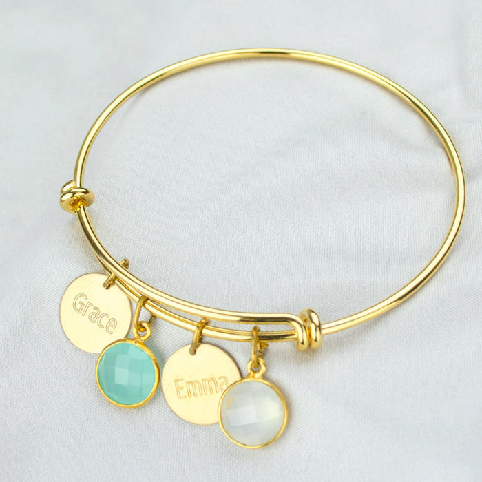 Single gold bangle bracelet with two name disks and an aqua chalcedony and moonstone birthstones with names engraved in modern thin font