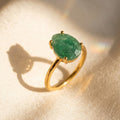 Natural teardrop emerald ring with faceted green gemstone in a yellow gold vermeil prong setting on warm cream fabric.