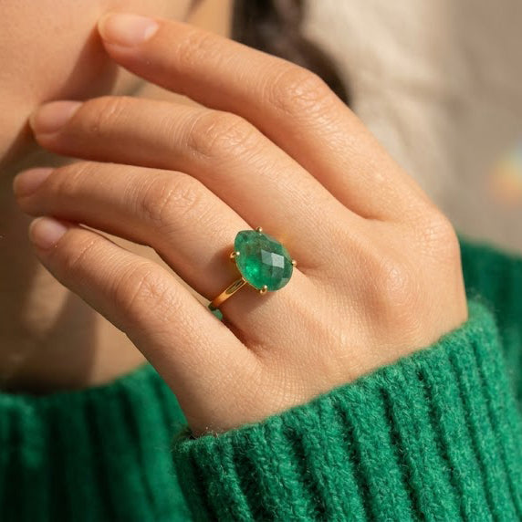 Woman wearing a natural emerald teardrop ring in yellow gold, showing the green May birthstone’s size and hand scale.