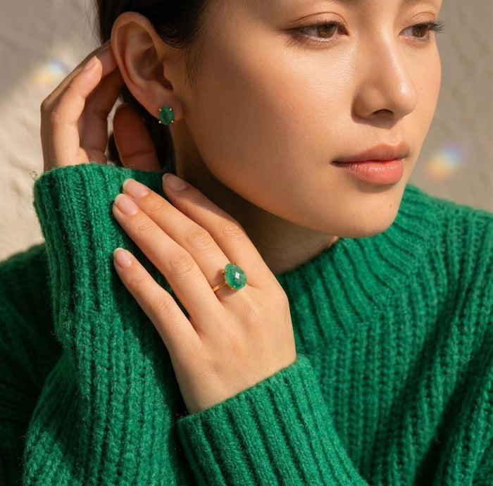Woman wearing a teardrop emerald ring with matching green gemstone earrings, styled with a rich emerald sweater.