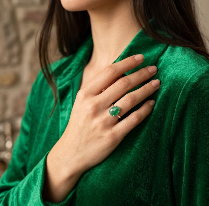 Woman wearing the natural emerald ring with a green blouse, showing the teardrop gemstone in an elegant lifestyle setting.