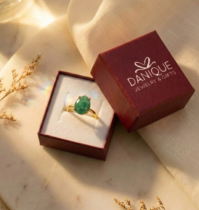 Natural emerald teardrop ring displayed in a Danique Jewelry gift box beside branded packaging and dried flowers.