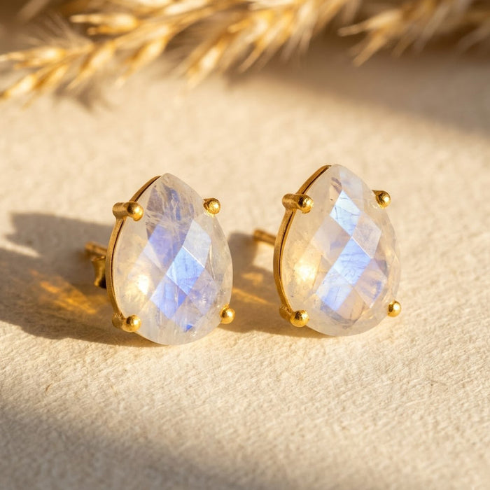 Natural rainbow moonstone teardrop stud earrings in yellow gold, shown in warm sunlight with soft blue and white flashes for June birthstone jewelry.