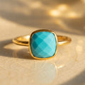 Natural turquoise cushion ring in gold shown close up in warm sunlight.