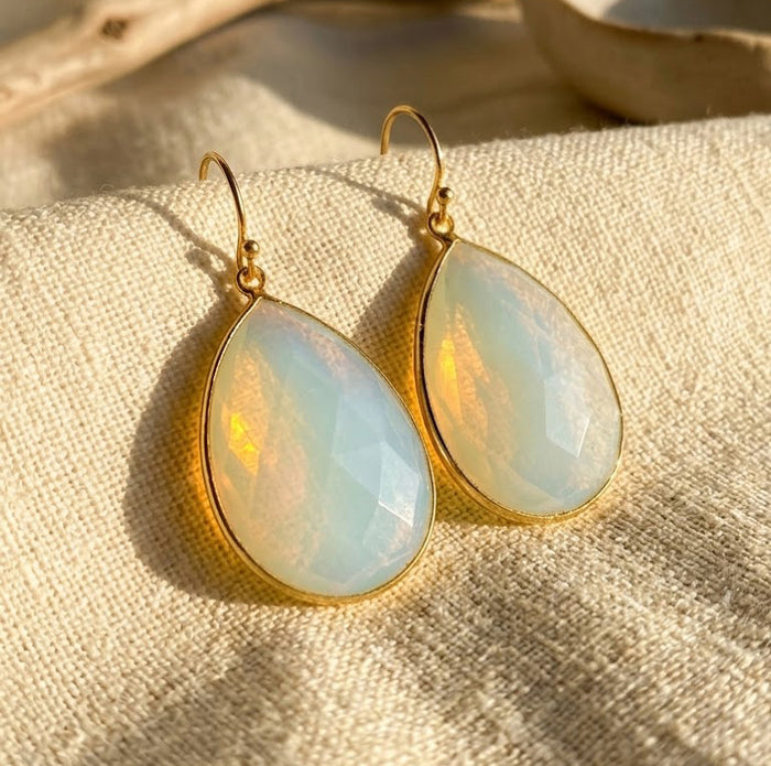 Opalite teardrop earrings in yellow gold vermeil displayed on cream fabric in warm natural sunlight.