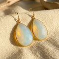 Opalite teardrop earrings in yellow gold vermeil displayed on cream fabric in warm natural sunlight.